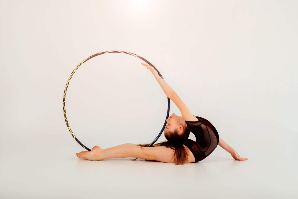 A girl gymnast in a black leotard with a with hoop on a white background. Rhythmic gymnastics concept